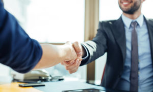Two men in suits shake hands in an office setting.