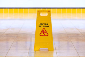 A yellow wet floor sign inside of a building with tiled flooring